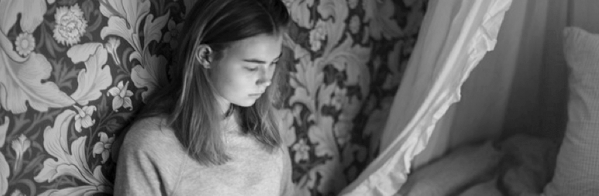 En tjej sitter på en säng med en dator i sitt knä.